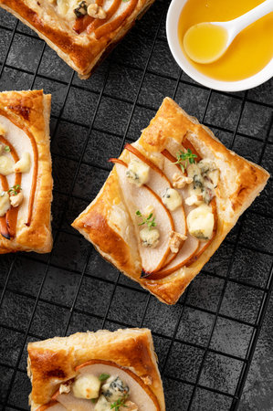 Mini tarts with puff pastry, pieces of pear, blue cheese, walnuts and honey on a concrete...