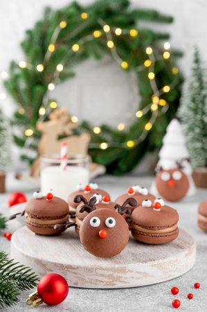 Christmas chocolate macarons in the form of deer on a wooden board on a concrete background. Festive dessert. Top view, copy spaceの写真素材