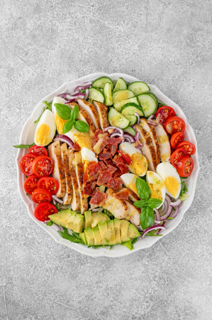 Healthy cobb salad with roasted chicken breast, chopped avocado, tomatoes, bacon, cucumber, hard boiled egg and green leaves on a plate. Top viewの写真素材
