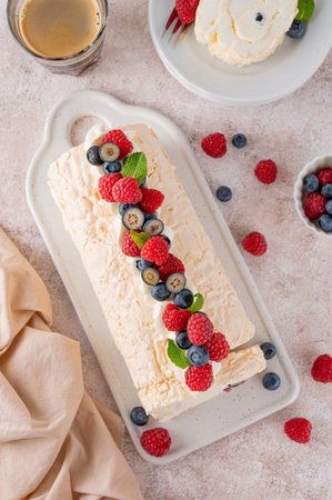 Meringue Pavlova roll cake with cream and fresh berries on top on a ceramic board on a concrete background. Copy spaceの写真素材