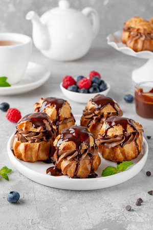 Profiteroles with chocolate cream, fresh berries and chocolate glazed on a plate on a gray concrete...