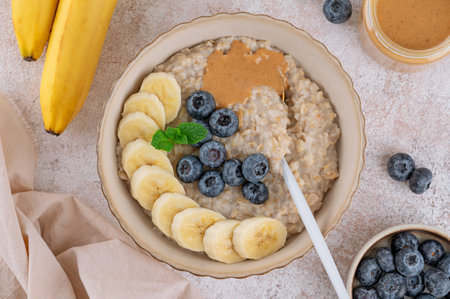 Oatmeal with milk, berries, sliced banana and nut butter in a bowl on a concrete background. Healthy breakfast. Top viewの写真素材