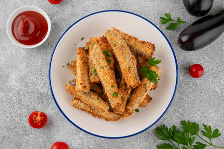 Baked crispy eggplant sticks served with tomato sauce on a plate on a gray concrete background. Vegetarian healthy dish. Selective focus.の写真素材