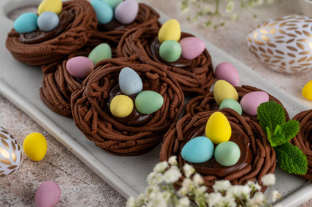 Easter chocolate nest cookies with chocolate cream and colorful candy eggs on a white ceramic board....