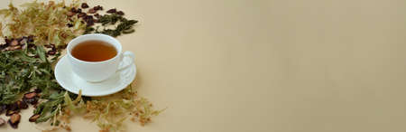 Banner whith herbal tea in a white cup for beauty and health, dried linden flowers, herbs and strawberries lie around.の写真素材