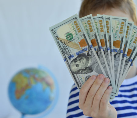 A young man in a striped vest holds hundred-dollar bills in his hands against the background of a...