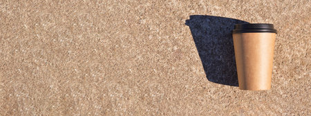 A wild banner whith a brown cardboard disposable coffee cup with a black plastic lid, which stands...