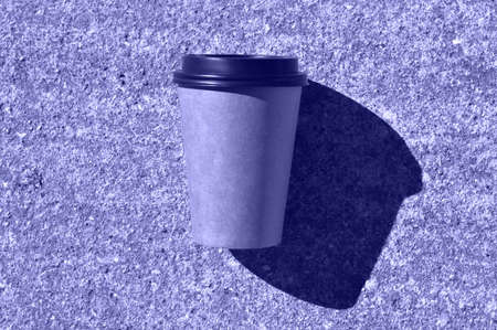Very pery cardboard disposable coffee cup with a black plastic lid, which layss on a concrete path and casts a hard shadow. A place for your packaging design.の写真素材