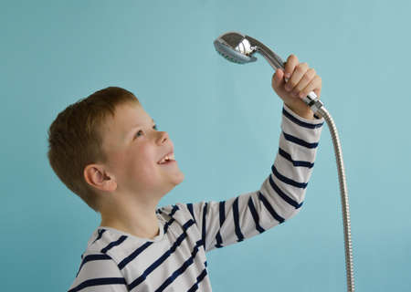 A happy smiling boy with a watering can from the shower over his head on a blue background. The concept of housewarming, renovation, happy childhood. Place fo text.の写真素材