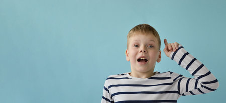 Wild banner an attractive Caucasian 9-year-old boy dressed in a striped longsleeve raises his index...