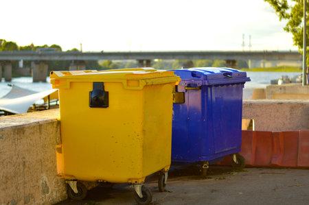 Yellow and blue garbage bin stand on the embankment in the city. Public trash on the side of the...