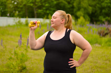 Portrait of cheerful aged plus size woman in fitness wear exercising with yellow dumbbells in park. Fitness, sport and healthy lifestyle conceptの写真素材