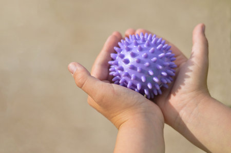 Close-up of a child's hands holding a purple prickly antistress ball. Performs exercises for the development of fine motor skills, sensory sensations, coordination of movements.の写真素材