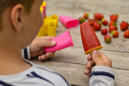A view over the shoulder of a cheerful Caucasian boy who opened homemade homemade ice cream made from strawberries.の写真素材