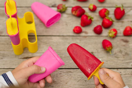 Top view of children's hands that opened homemade homemade ice cream on the background of a wooden table with strawberries.の写真素材