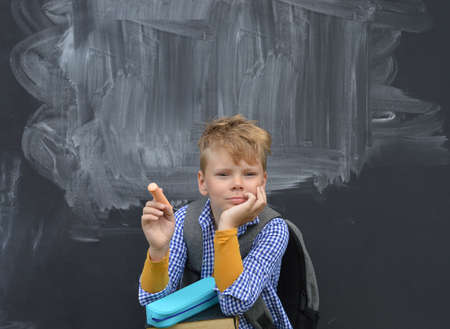 Caucasian boy sitting with chalk in hand. Disheveled against a blackboard, thinking. back to school.の写真素材