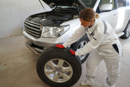 A female car mechanic in a white worker replaces a wheel on a car at a service center. Car...