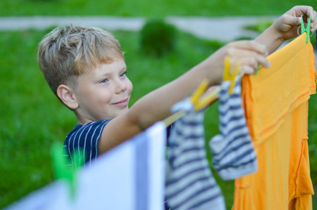 A happy caucasian 9 years boy helps her mother to hang up clothes. Development of fine motor skills through household activities. selective focus.の写真素材
