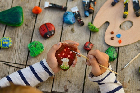 A detailed picture of a child's hands drawing a fungus on a stone with acrylic paints. Home hobbies...