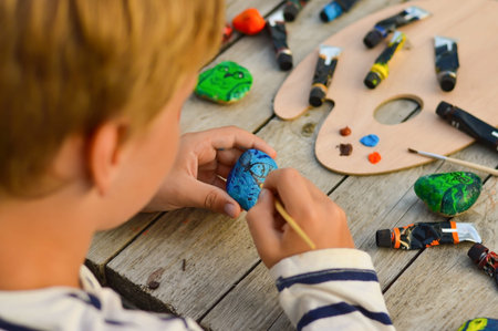 A detailed picture of a child's hands drawing a blue owl on a stone with acrylic paints. Home hobbies are authentic. Artwork on stones.の写真素材