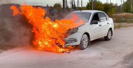 Accident. A white car in an industrial area is on fire. The engine compartment is on fire