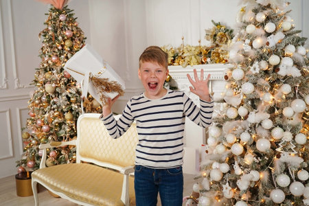 Portrait of a happy Caucasian boy holding a Christmas gift in his hands, against a background of lights. Waiting for a miracle, childhood.の写真素材