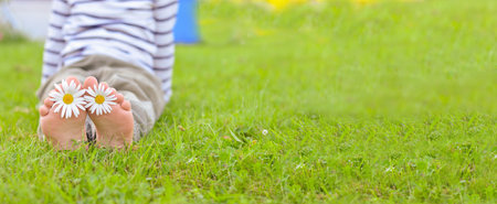 A child is sitting on the green grass in the park in summer with daisies between his toes. Focus on the legs.の写真素材
