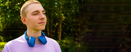 Banner, Portrait of a teenager in a purple sweatshirt with headphones, smiling in the park on a...