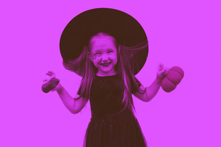 Tinted image. Portrait of a little girl in a witch costume with a spider web pattern on his face and a pumpkin in his hands.の写真素材