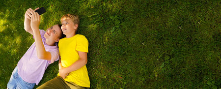 Two happy brothers lying on green grass in meadow with cellphone. children looking at mobile phone...