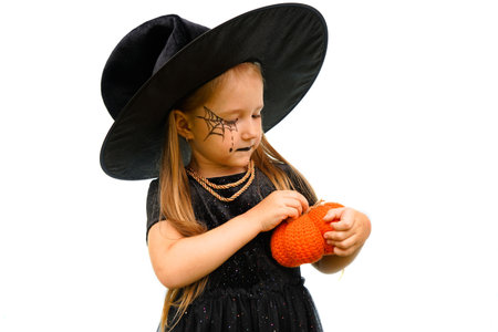 Portrait of a little girl in a witch costume with a spider web pattern on his face and a pumpkin in...
