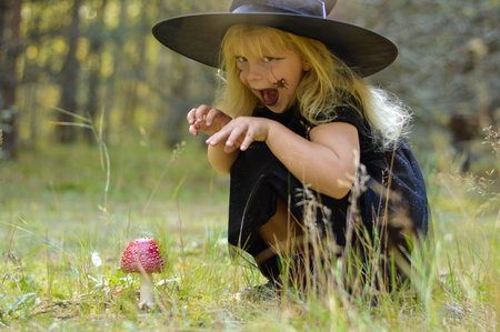A girl in a witch costume and a black hat collects fly agarics in the forest to make a potion. Magic, Halloween.の写真素材