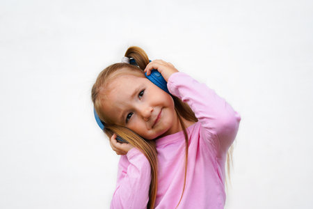 Carefree attractive girl with blond short hairstyle, listening music in headphones, holding mobile phone, standing over white backgroundの写真素材