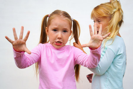 Cheerful little girls, sisters wearing casual style clothes isolated on white studio background. Emotions, happiness. Concept of childhood, family, studyの写真素材