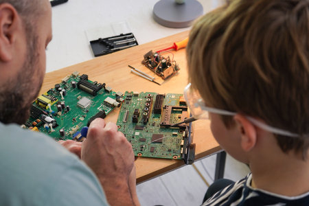Father with his son spend time together. Close-up of a man teaching his boy at home to solder computer spare parts. Education moment during parenthood. Togetherness concept.の写真素材