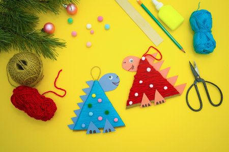Christmas tree toys a dinosaur made by a child out of cardboard and threads lies on a yellow background. The symbol of 2024. Educational and craft activity.の写真素材