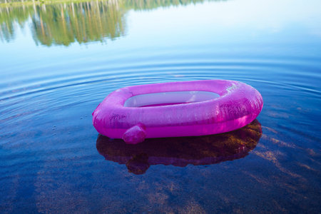 A pink children's swimming circle on the water of a calm lake.