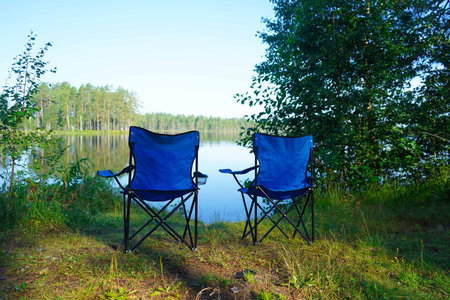 empty blue folding garden chairs on the shore of the lake on a sunny day