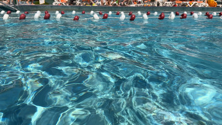 Blue water in the swimming pool and the legs of unrecognizable people who are walking.