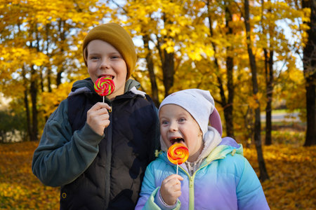 Portrait of a boy and a girl eating lollipops in an autumn park.の写真素材
