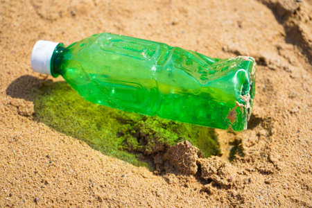 Plastic bottle on sandy beach. Empty uncapped used plastic drinking water bottles piled up with sand, dumped on the beach with copy space. Polluted garbage abandoned by tourists.の写真素材