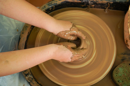 The potter's wheel. A close-up of the hands of a craftsman skillfully working with clay on a potter's wheel, giving it the shape of a clay productの写真素材