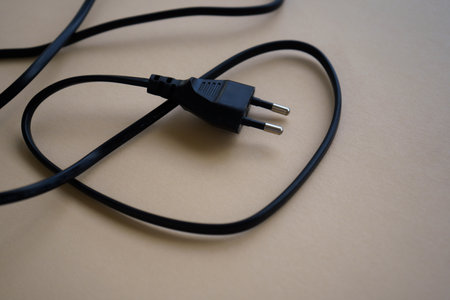 Electric European plug isolated on beige background. Black power cable with plug. Power cord close-upの写真素材