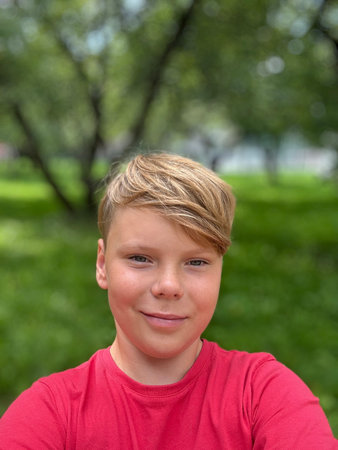 An eleven-year-old guy in a red T-shirt takes a selfie on the streetの写真素材