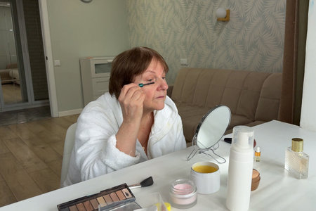 A lovely senior lady is at her residence, applying makeup with care.の写真素材