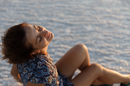 happy smiling girl enjoying the sunset sun and shakes her head, sits on the saltの写真素材