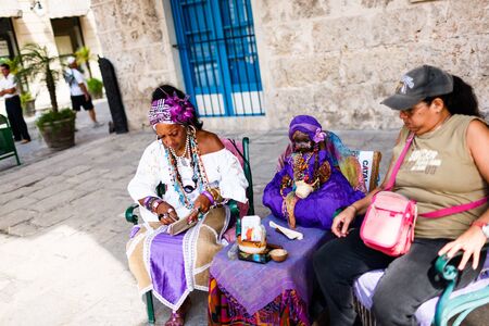 Dark-skinned Cuban in white costume tells fortunes to tourists in Havana streetsのeditorial素材