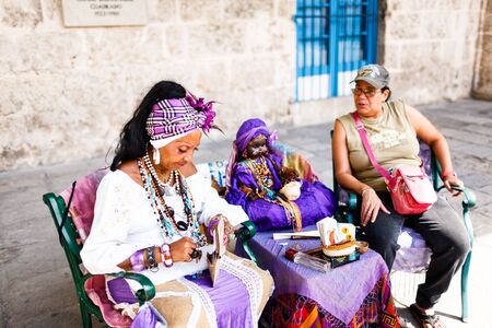Dark-skinned Cuban in white costume tells fortunes to tourists in Havana streetsのeditorial素材