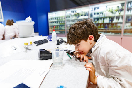 An 8-year-old boy in a white lab coat conducts an experiment, observes the decomposition of color into composite base colors, awaits the result, puts his head in his palmのeditorial素材