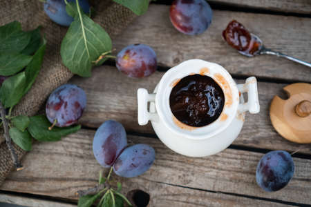 plum jam in a white ceramic pot on an aged wooden background, fresh plums nearの写真素材